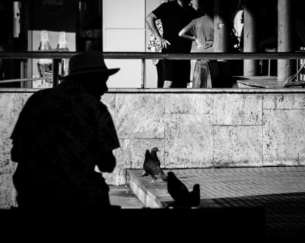 Black and white street scene with a man feeding pigeon in Bucharest Romania